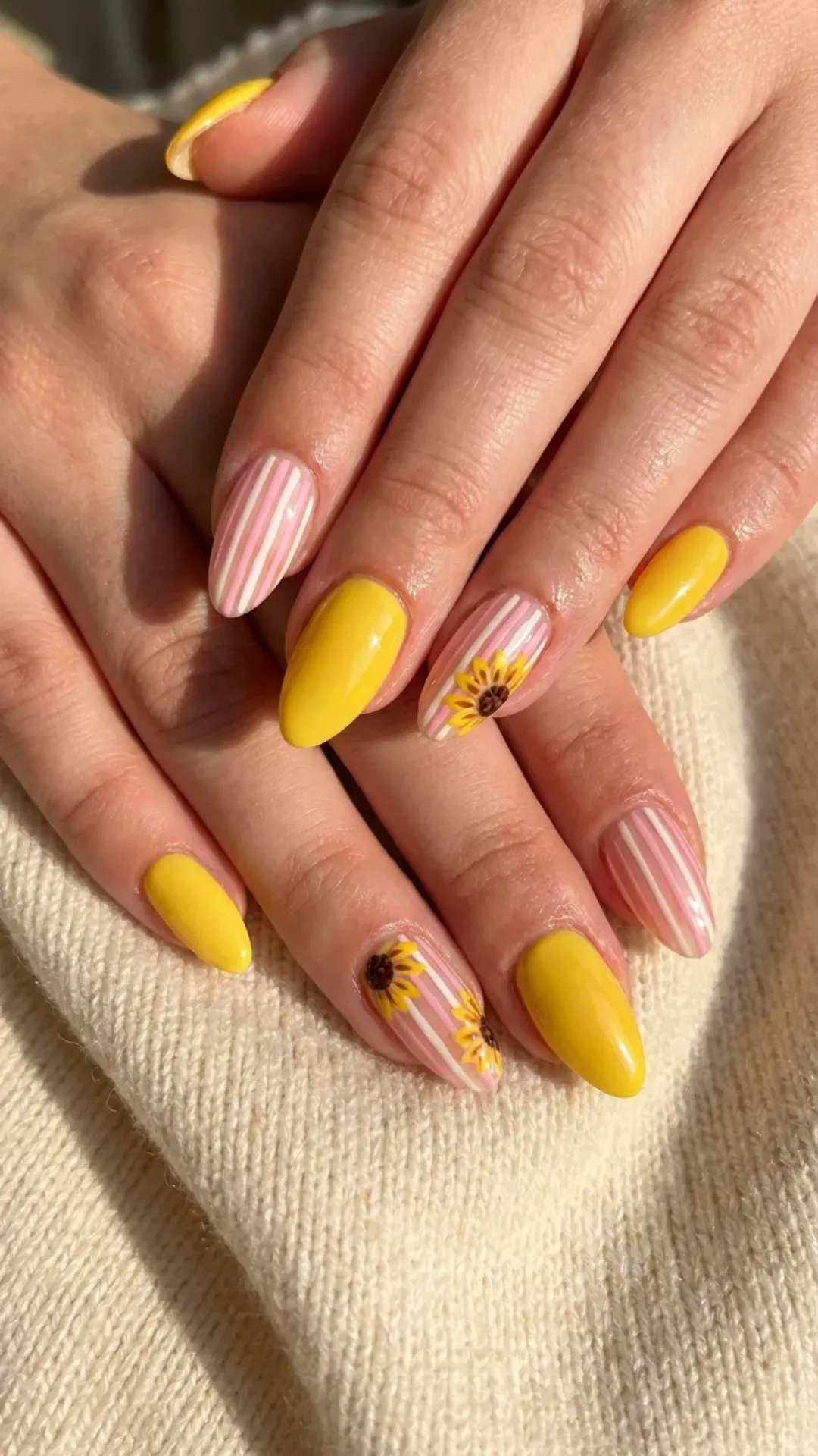 Bright yellow nails alternated with pink-striped ones, some adorned with delicate sunflower designs, creating a sunny and cheerful nail art look.