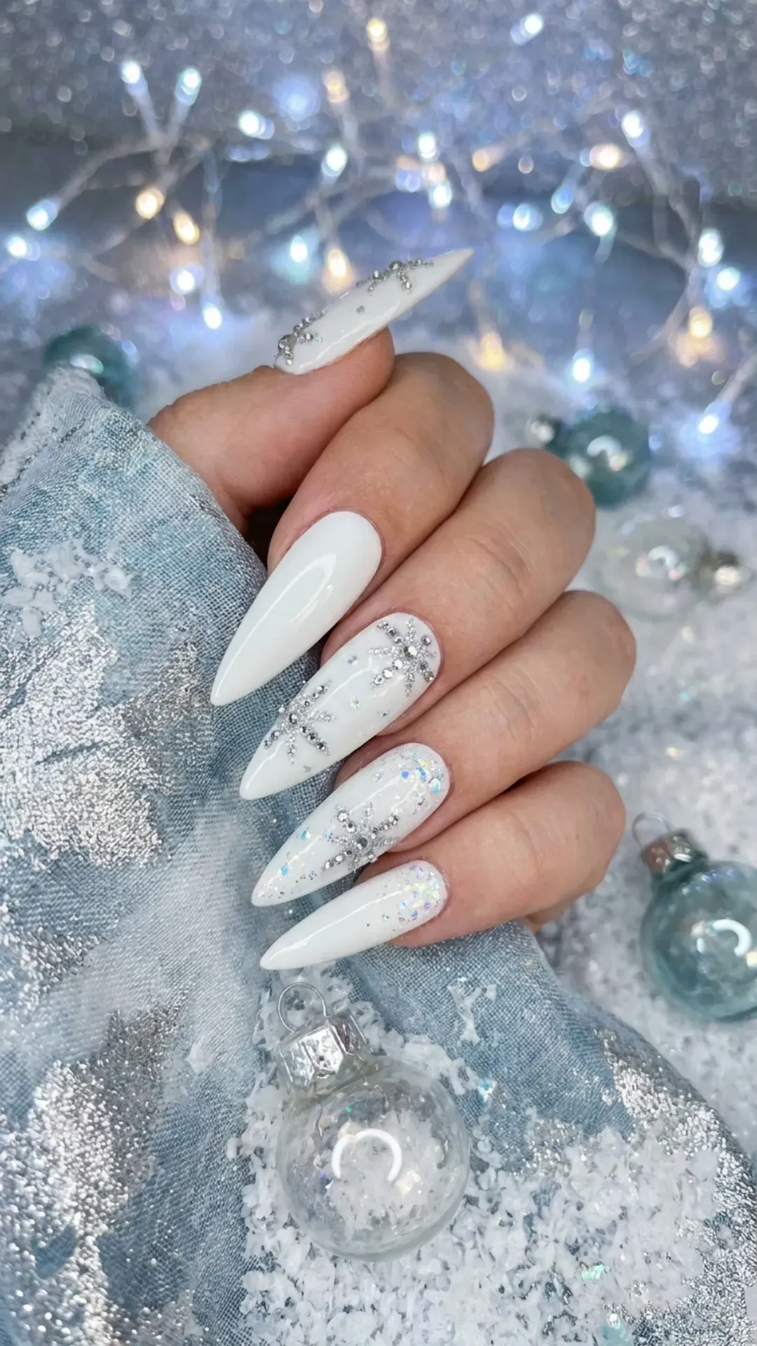  Luxurious stiletto nails featuring white polish with intricate rhinestone snowflake designs and glitter, embodying a dazzling winter wonderland aesthetic.