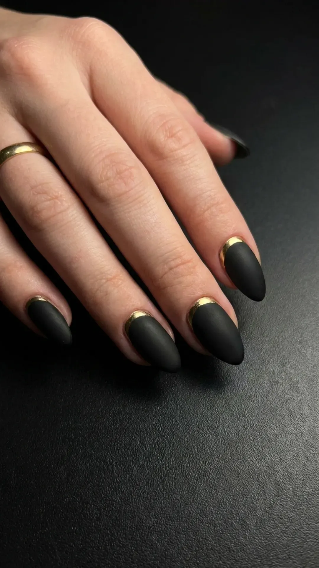 Striking matte black nails with a glossy gold crescent design near the cuticle, combining boldness and elegance in a modern fashion statement.