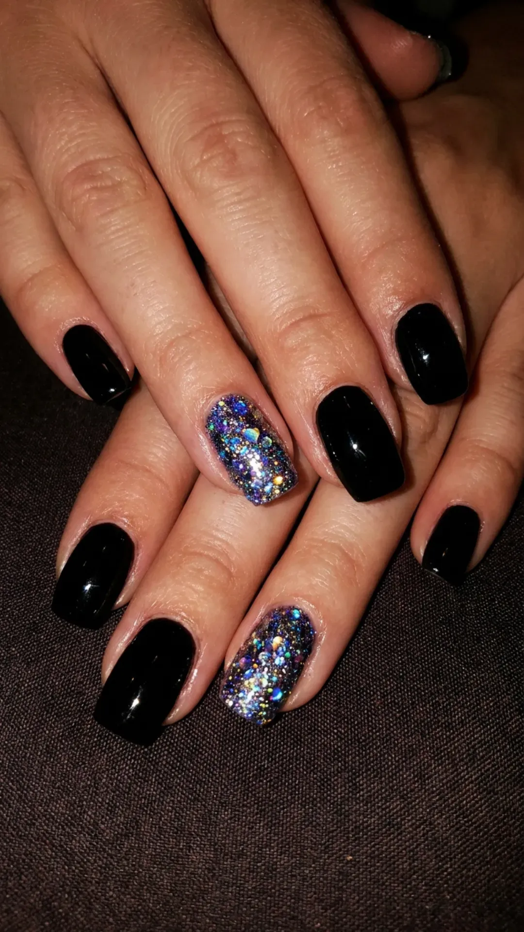 Captivating black nails intermixed with holographic glitter, reflecting a spectrum of colors reminiscent of a starry night sky.