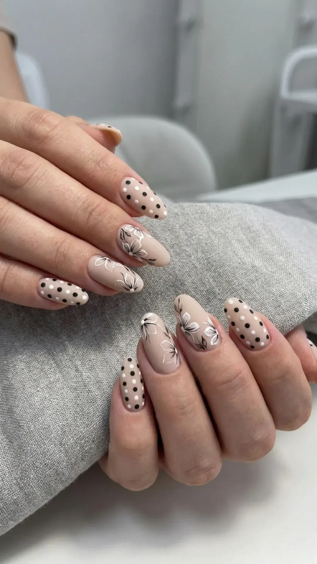 A monochrome nail design with a mix of white, black polka dots, and floral accents, creating a playful yet elegant nail art on a neutral 