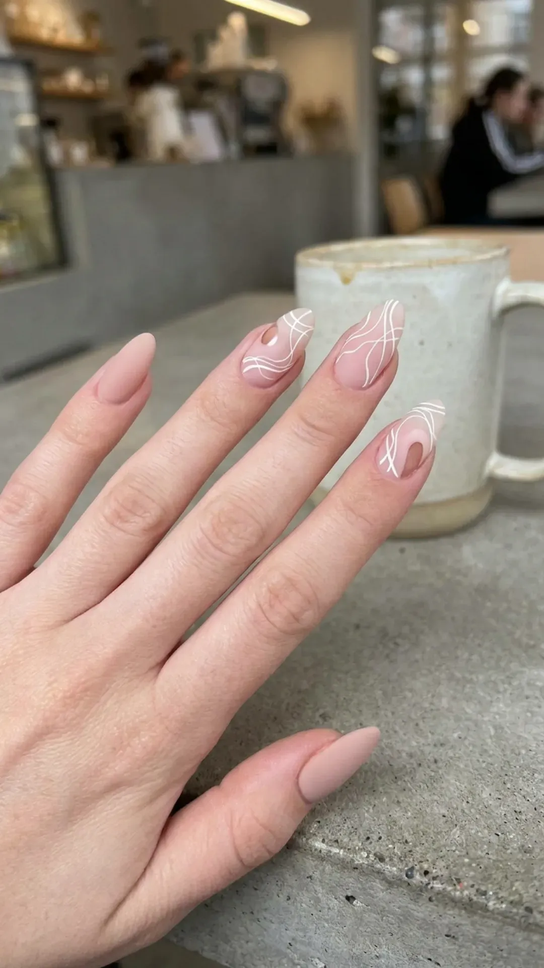 Trendy nude pink nails incorporating negative space with white abstract lines for a minimalist yet edgy manicure.