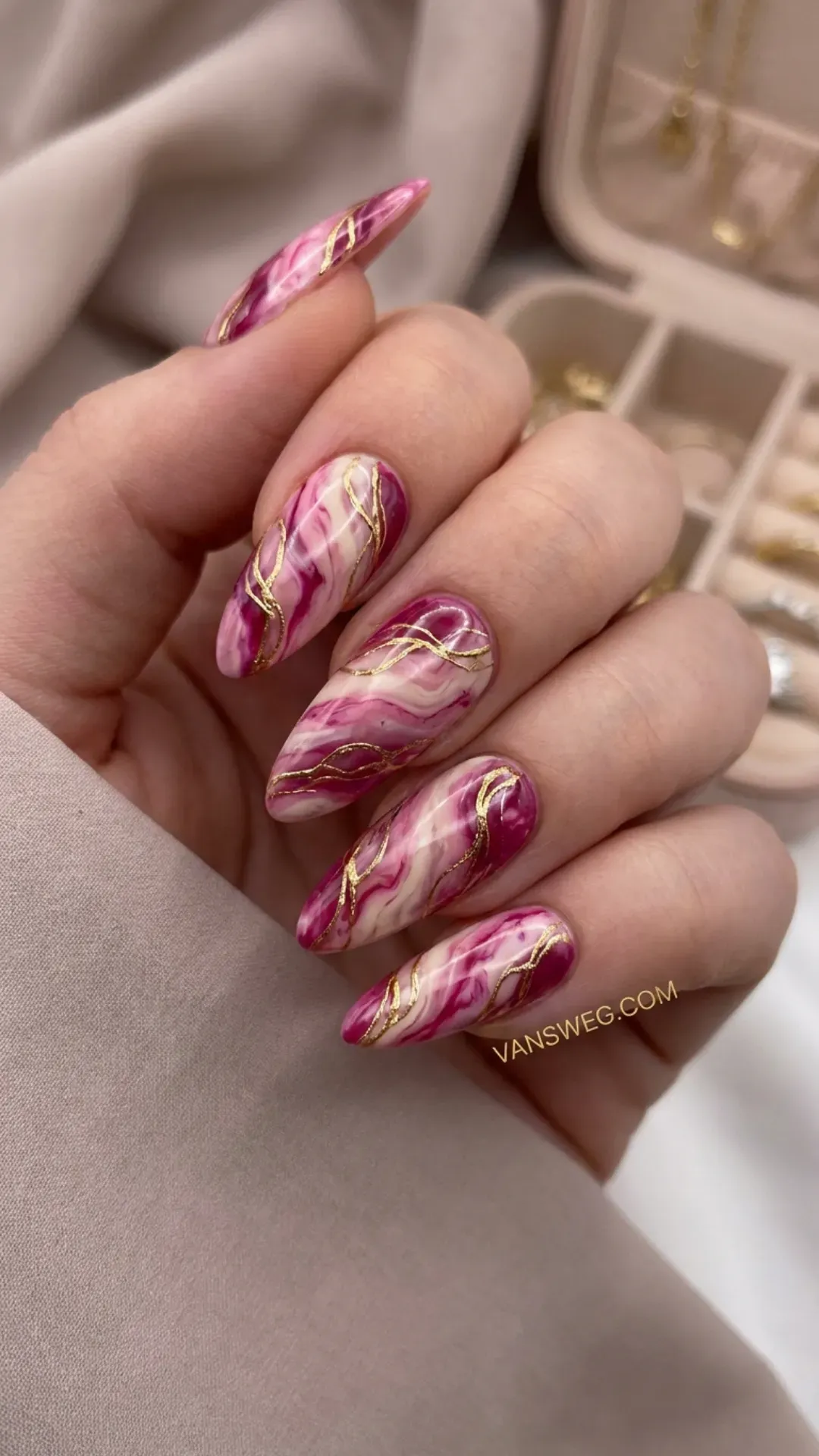 Long almond nails featuring an intricate pink, magenta, and white marble stone swirl design with gold lines by VANSWEG.COM.