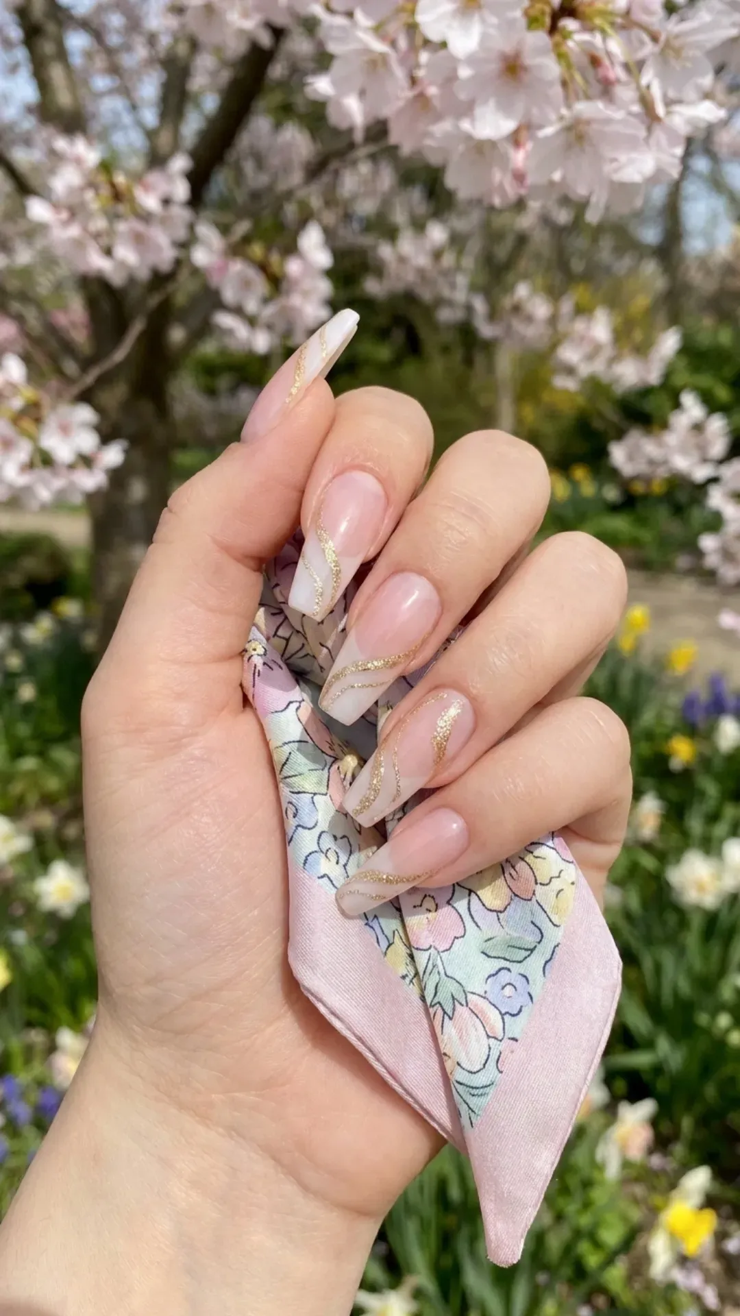 Chic white coffin nails with a sheer pink overlay and a captivating gold glitter swirl design, merging classic elegance with a touch of sparkle for the spring season