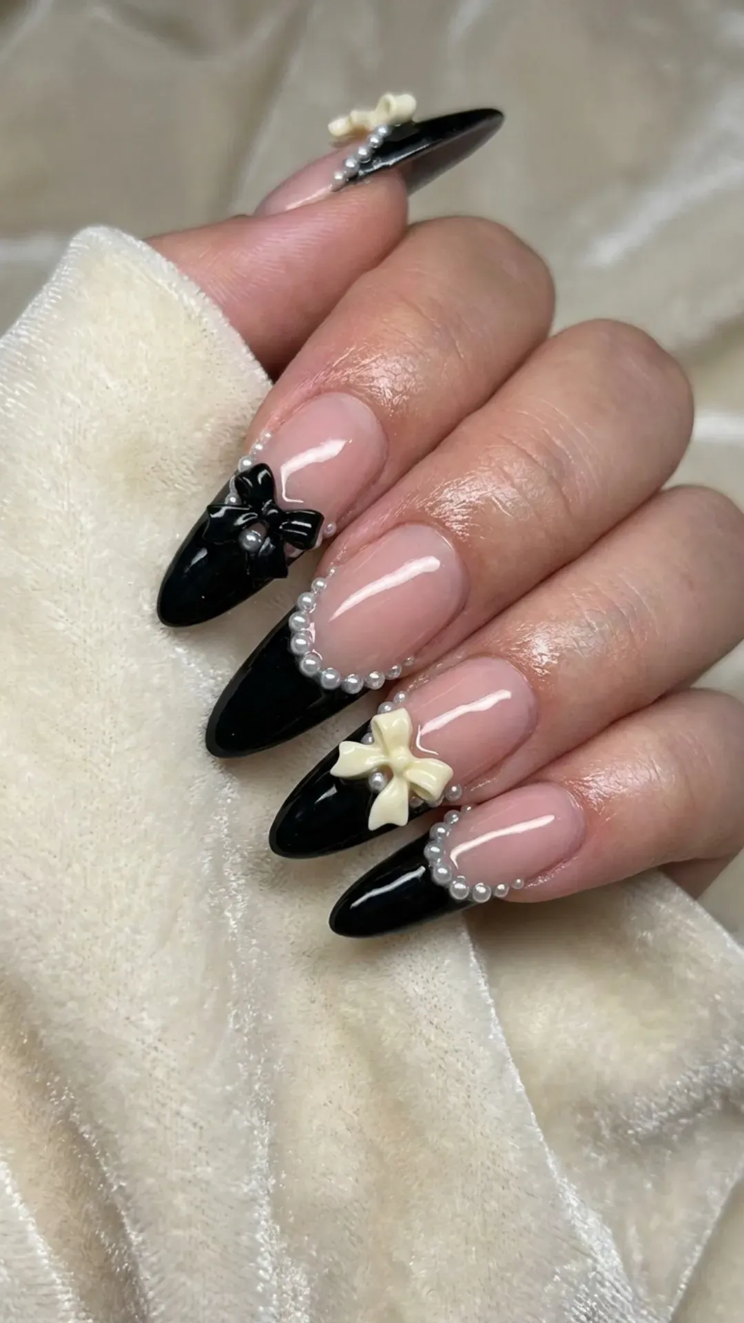 Black French tip nails decorated with 3D bows and pearl outlines, creating a luxurious and detailed manicure.