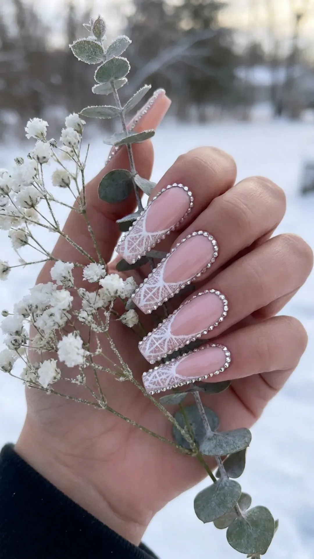 These elegant coffin nails are artfully decorated with a white lace design over a soft pink base, and framed with a crystal rhinestone border for an exquisite winter wedding nail look.