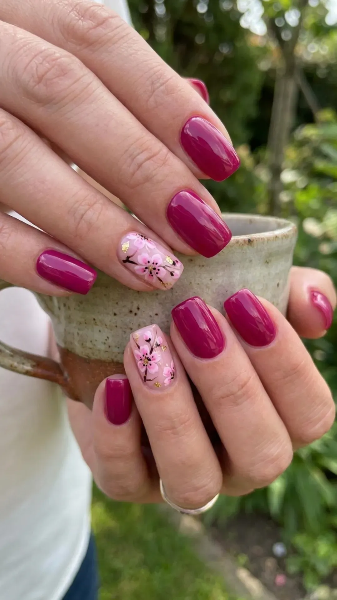 Rich fuchsia-colored nails with a glossy finish, featuring a single accent nail on each hand with delicate pink cherry blossom designs.