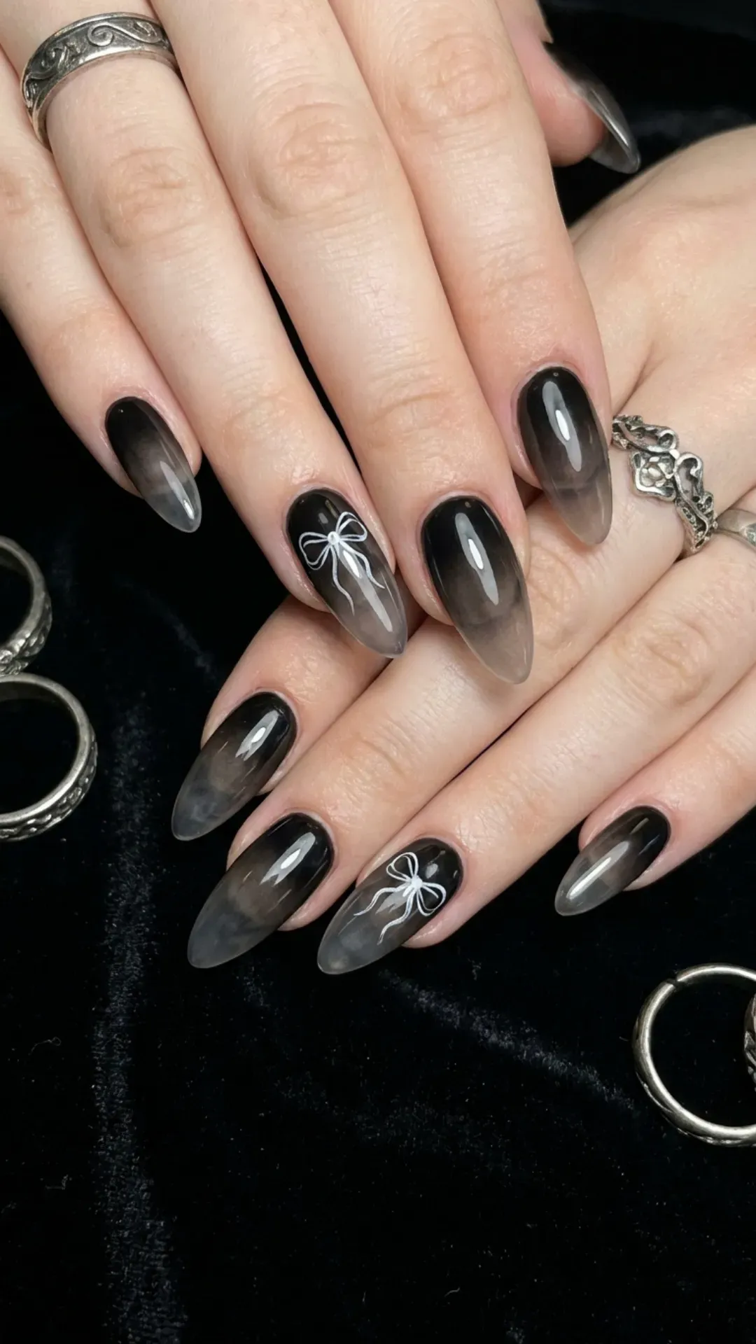 Black aura nails with a subtle faded effect and delicate hand-drawn bows for a mysterious and stylish finish.