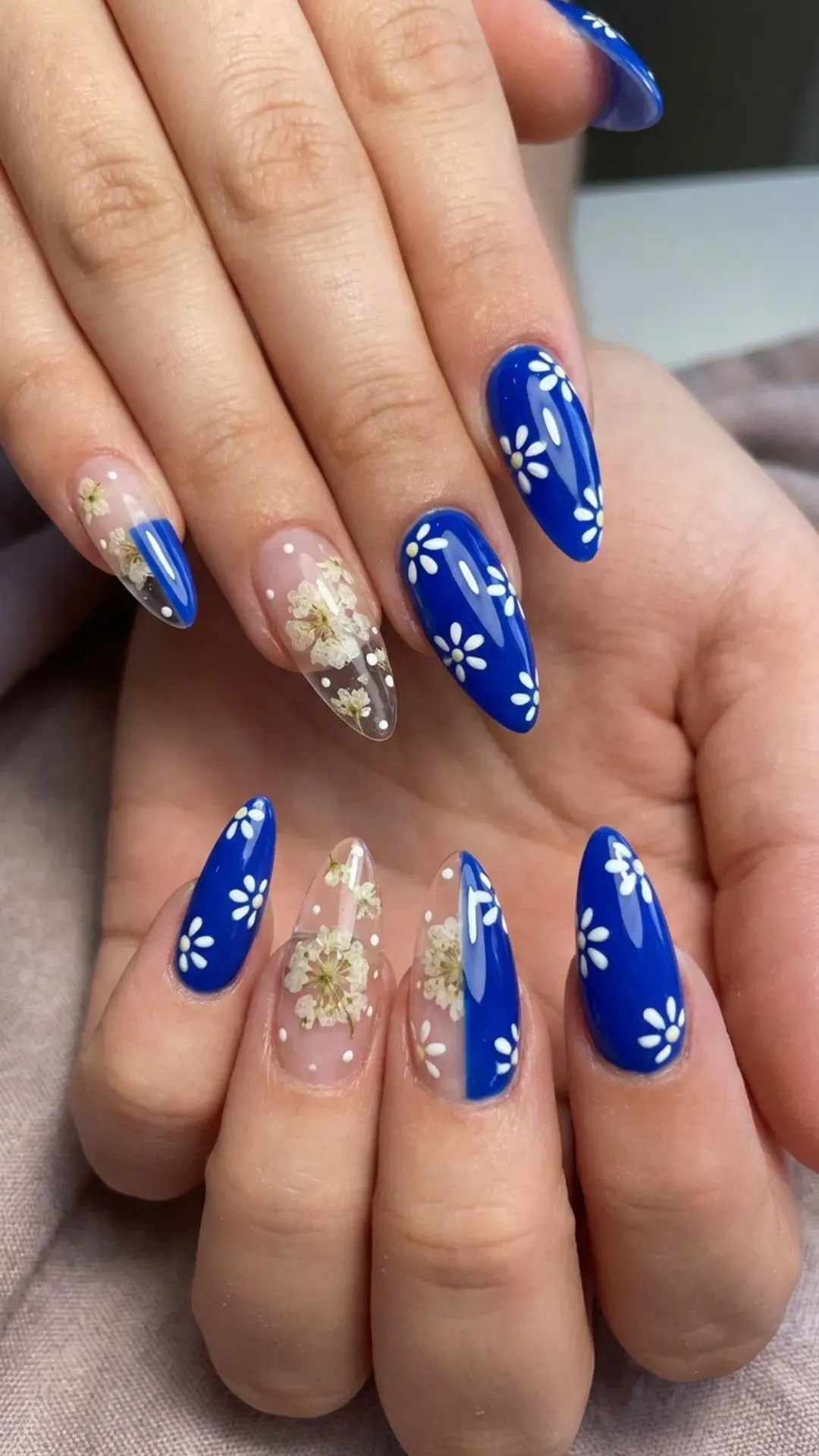A striking combination of royal blue and transparent nails, dotted with small white flowers for a bold yet delicate floral nail art statement.