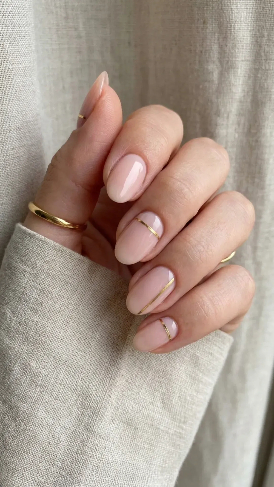 Soft nude pink nails enhanced with thin golden stripes, adding a simple yet elegant metallic accent for a refined appearance.