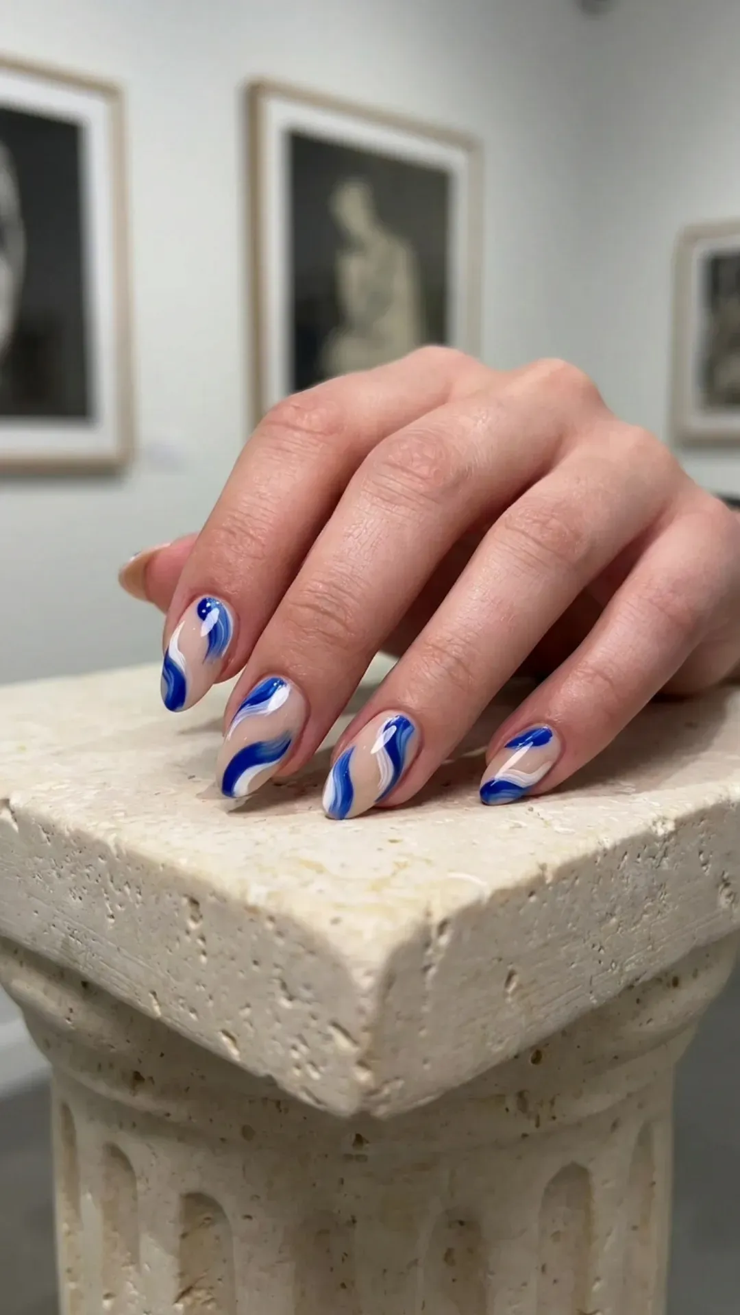 Medium almond nails with hand-painted cobalt blue and white abstract brushstroke art on nude base — editorial summer nails 2026