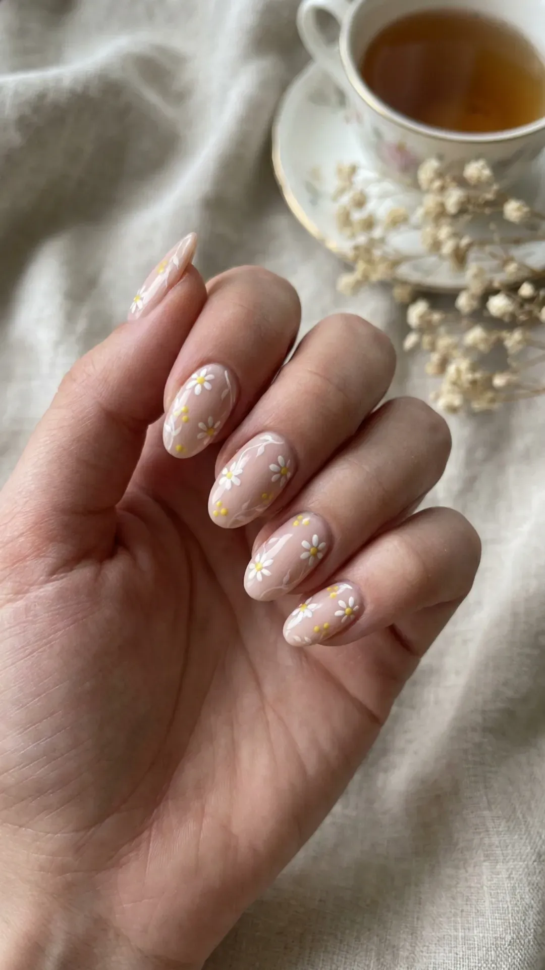 Soft pastel nude nails providing a perfect canvas for intricate white and yellow floral accents, creating a delicate and refined nail art design