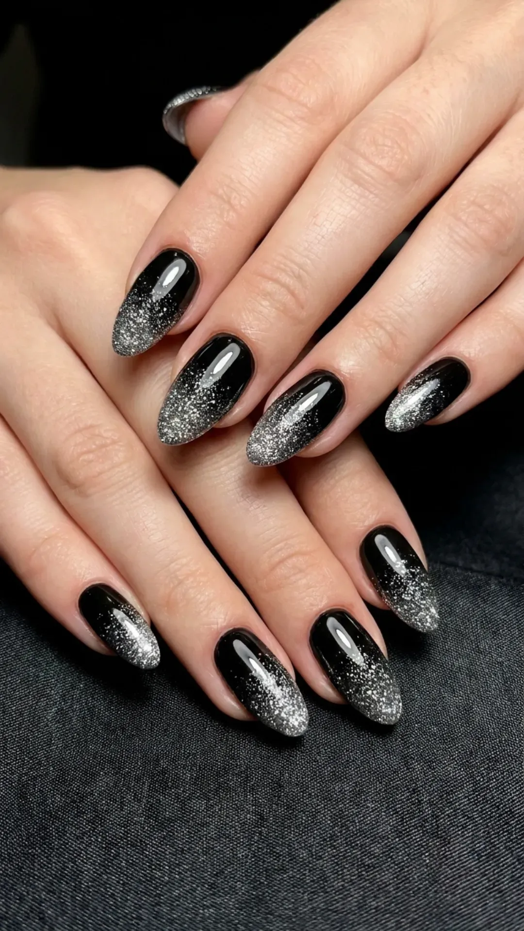 Stylish black nails with a seamless glitter ombre effect, transitioning from a dense silver sparkle at the tips to a solid black base.