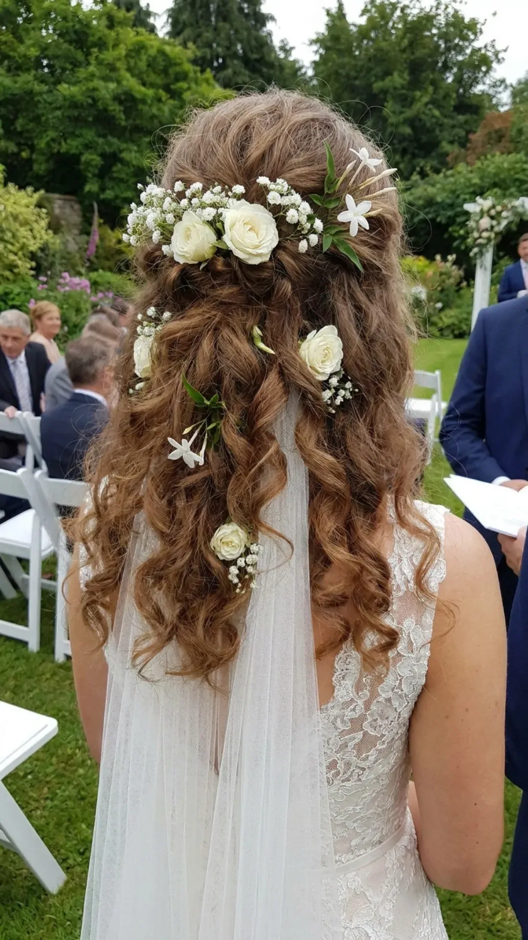 Voluminous curly half-updo accented with elegant white floral pieces, adding a romantic and refined touch to the bridal look, ideal for a heartfelt wedding ceremony.