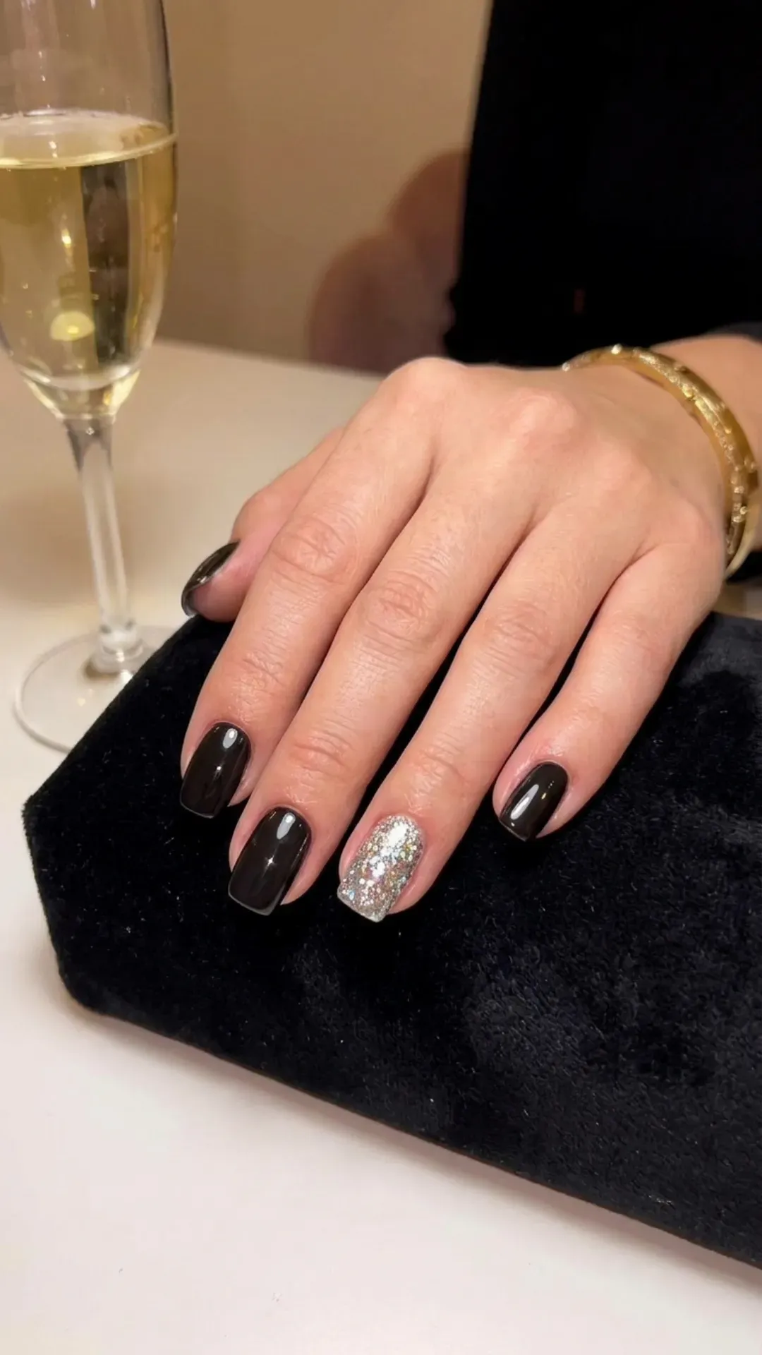 Sleek and shiny black nails with one statement nail fully coated in silver glitter, exuding a luxurious and opulent charm.