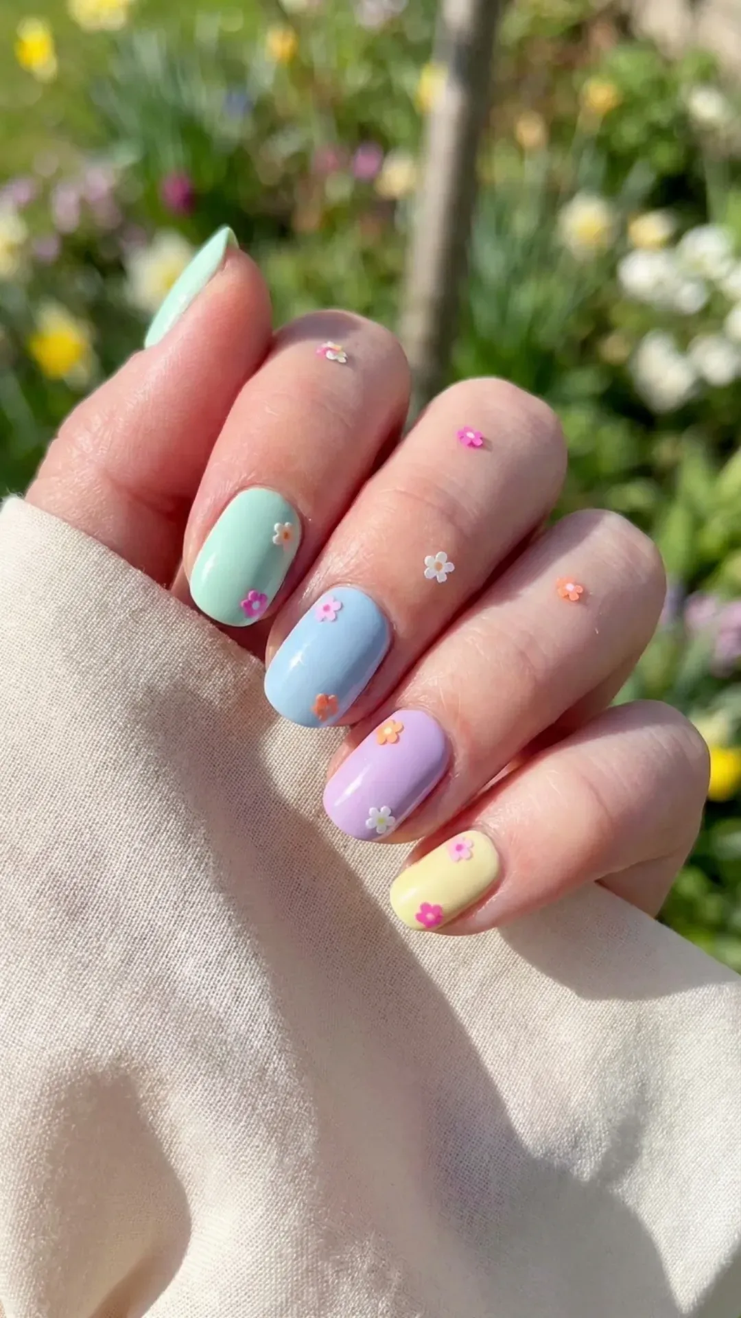 Pastel-toned nails sprinkled with colorful flower-shaped dots, creating a playful and candy-like effect ideal for a light-hearted spring look.