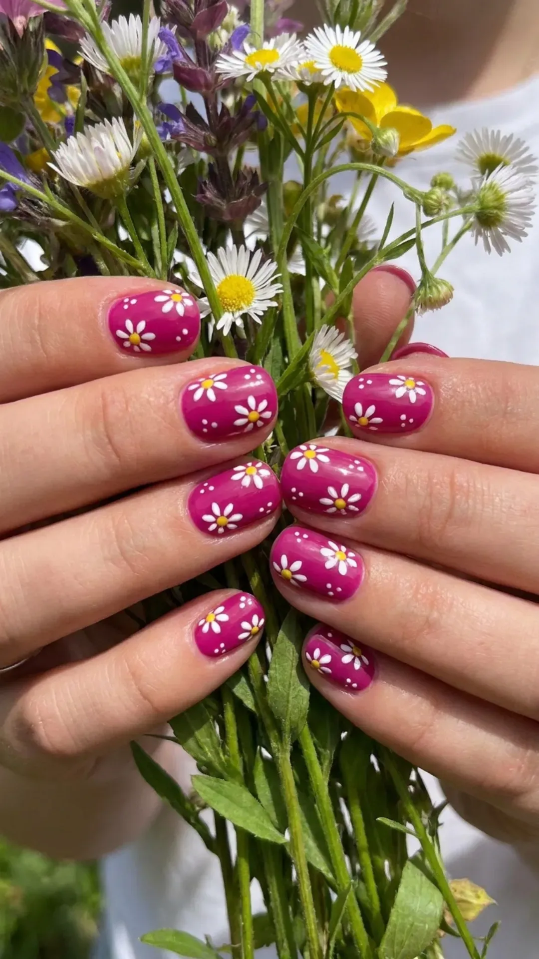 Curved short nails with a glossy fuchsia base featuring white daisy-like floral accents on each fingernail