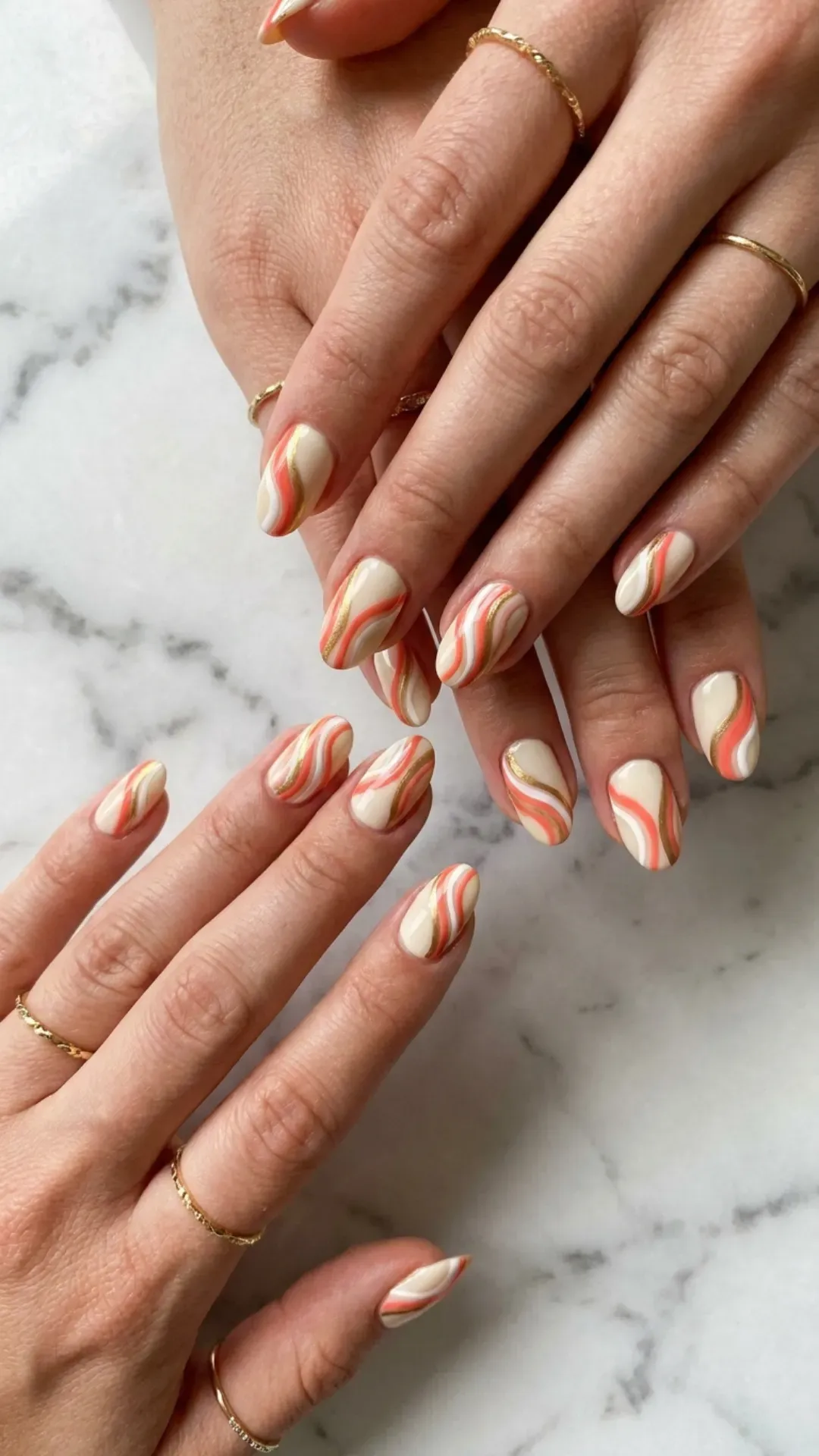 Medium oval nails with hand-painted coral, white and gold stripe and swirl patterns on cream base — summer nail art 2026
