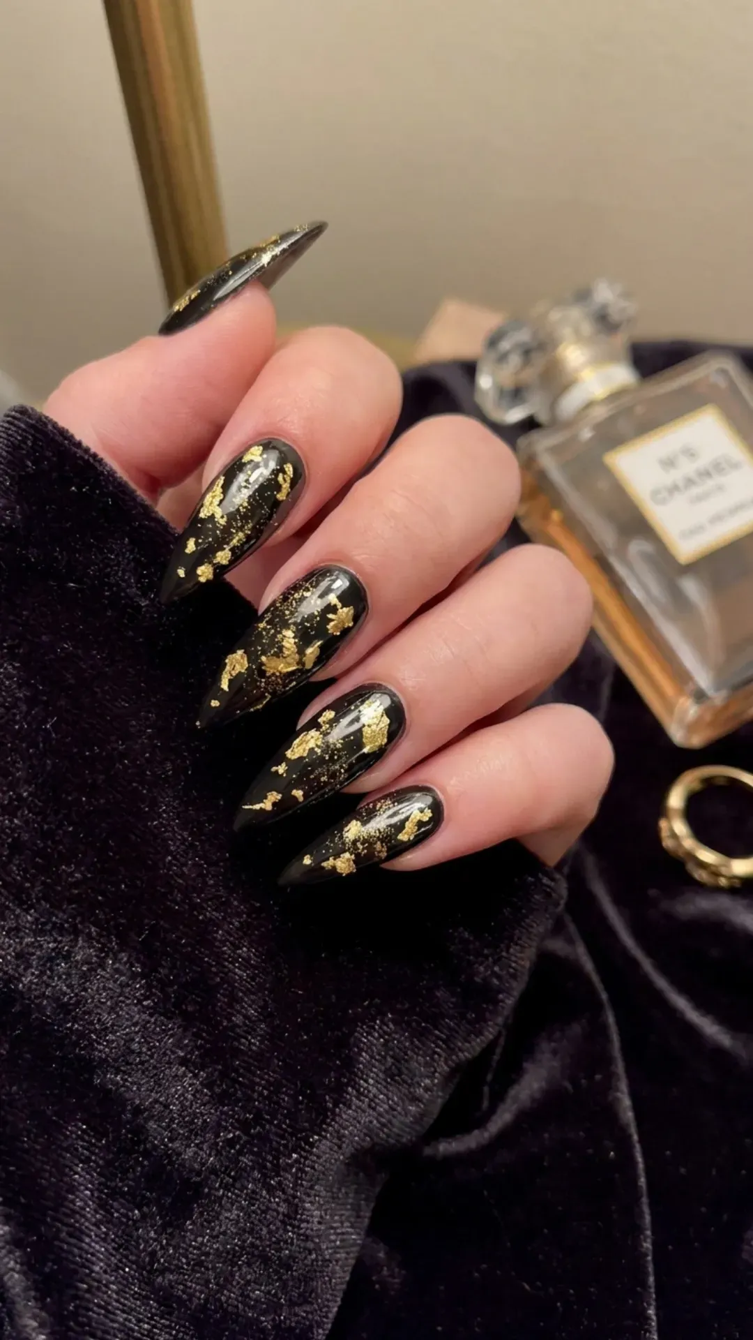 Stunning stiletto nails featuring a sleek black base with gold foil accents, evoking an elegant look with a touch of opulence.