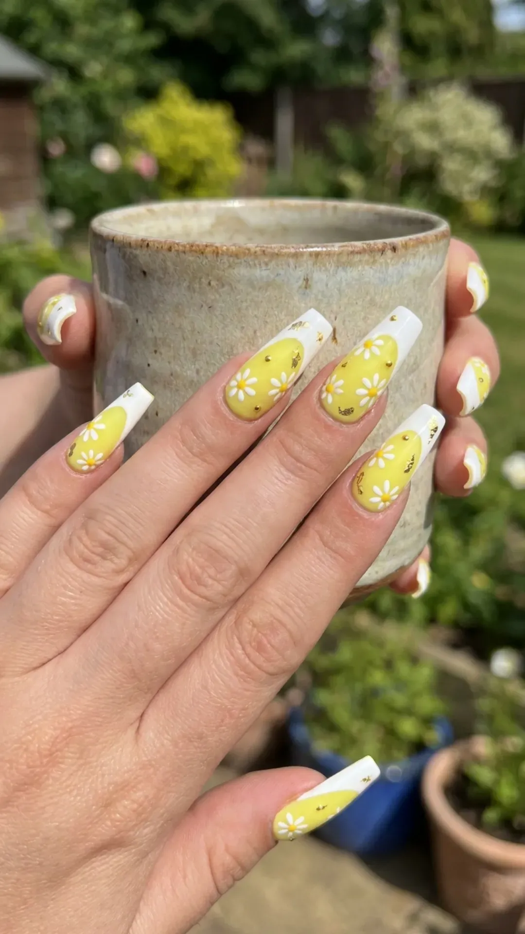 Coffin-shaped nails with a bright yellow and white French tip design, embellished with small white daisies and gold accents