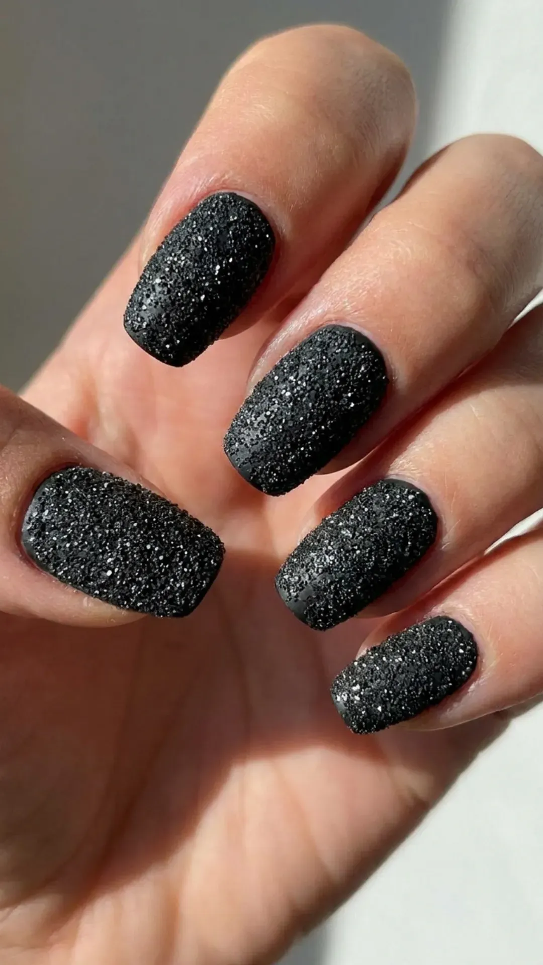 Black nails completely covered in fine glitter, resembling the textured surface of black sand, for a bold and gritty aesthetic.