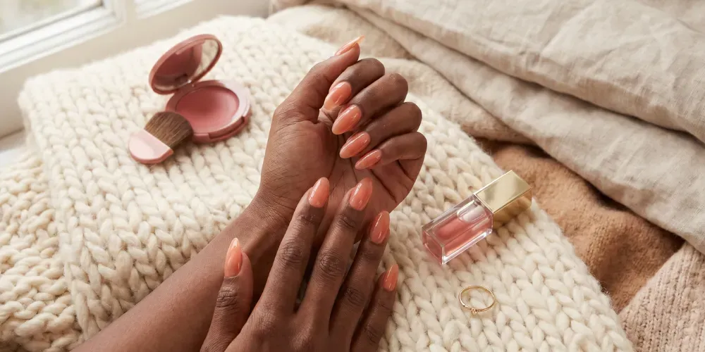 A cozy beauty flatlay highlighting minimalist lip gloss nails and the essential products needed for the sleepy girl blush trend.