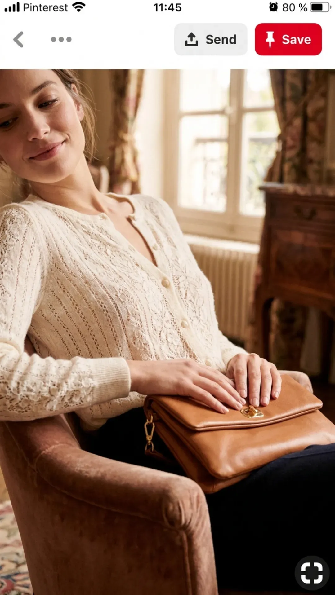 A woman wearing a soft ivory pointelle knit sweater with intricate details, holding a leather clutch bag.