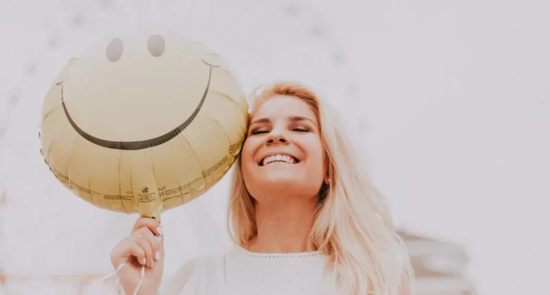 Woman smiling while undergoing a light therapy treatment, emphasizing self-care routines for emotional wellness.