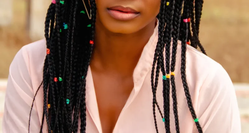 Woman with colorful beaded braids: "Black woman with long braided hair featuring colorful beads, wearing a light pink shirt, showcasing a modern hairstyle with traditional African influences."