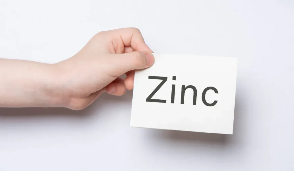 A person's hand holding a white card with "Zinc" written on it, symbolizing the importance of minerals in health or skincare.
