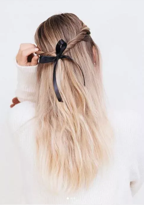 A casual yet trendy half-up hairstyle tied with a delicate black ribbon, showing off the beautiful texture of the blonde waves.
