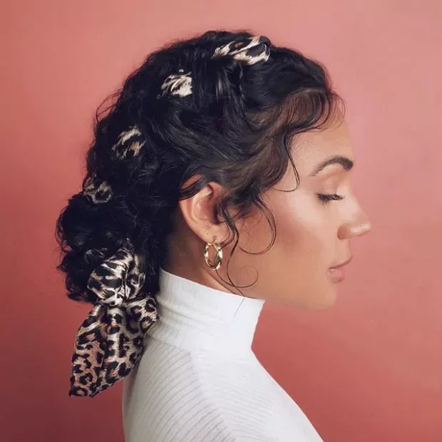 Side profile of a woman with a voluminous, curly ponytail secured with a leopard print scarf, giving a chic bohemian vibe.
