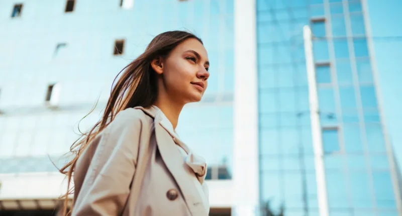 Confident woman walking outdoors, with modern buildings in the background, portraying urban professional lifestyle.