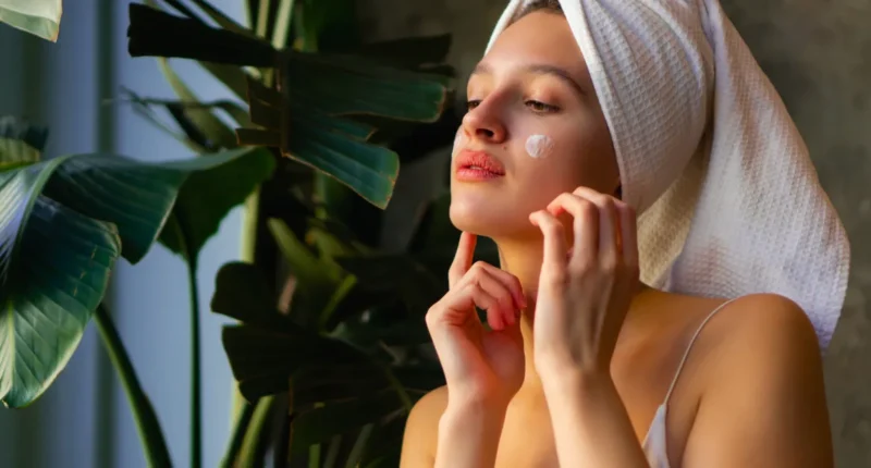 A serene image of a woman in a towel turban gently applying facial cream, illustrating a daily routine from the Top 10 Cold Weather Skin Care Tips for maintaining a healthy skin barrier against the chill.