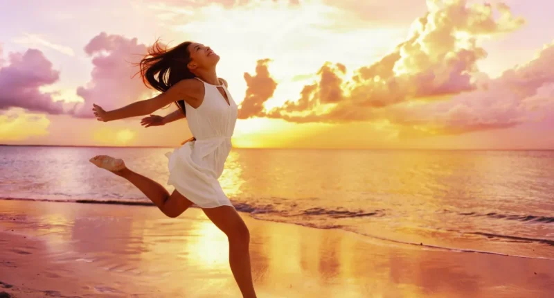 Happy woman jumping on the beach at sunset