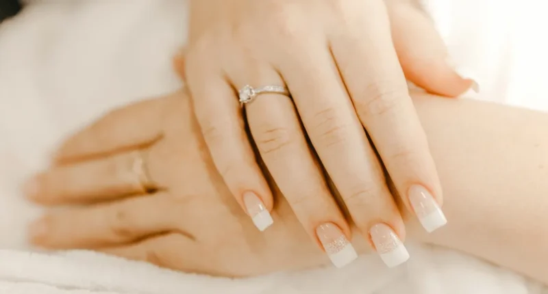 Close-up of a hand with a classic French manicure and a sparkling diamond engagement ring on the ring finger, symbolizing elegance and commitment