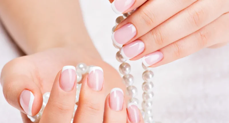 Close-up of hands with a classic French manicure, featuring a sheer pink base and white tips, elegantly complemented by a string of pearls