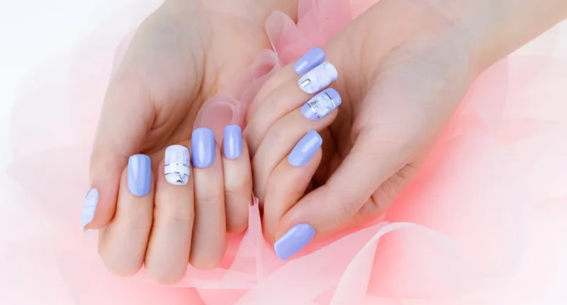 A pair of hands showcasing a chic nail design with soft lavender polish, complemented by marble patterns and silver foil accents, set against a delicate pink tulle background.