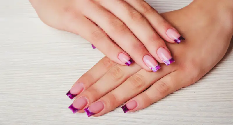 Creative French manicure featuring bold purple bow-tie designs at the tips of a soft pink base, adding a playful and charming twist to the traditional French tip for a fun spring look.