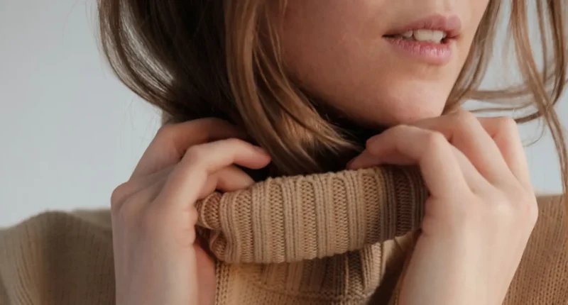 Close-up of a cozy caramel-colored turtleneck knit sweater being gently held by a woman, highlighting the soft texture and detailed weaves, a staple knitwear piece for the winter 2024 fashion season