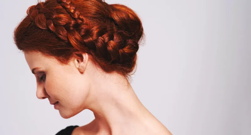 A regal crown braid updo on auburn hair, wrapping around the head to form a halo, perfect for an upscale evening event or a classical music concert