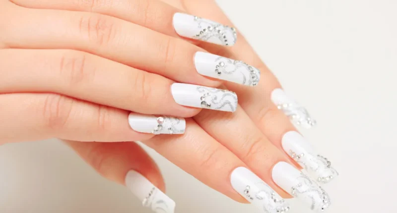 Long white winter nails with elegant silver glitter swirls and rhinestone embellishments, perfect for a sophisticated and festive seasonal look.