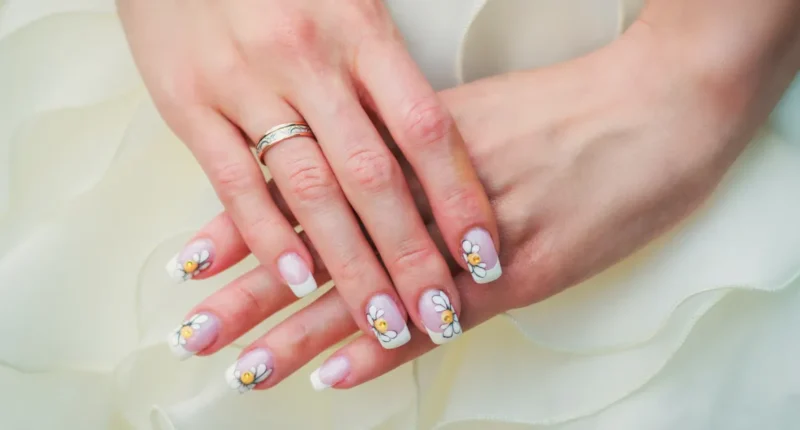 Elegant hand showcasing squared nails with a white tip, adorned with painted daisies and petals on a light pink base