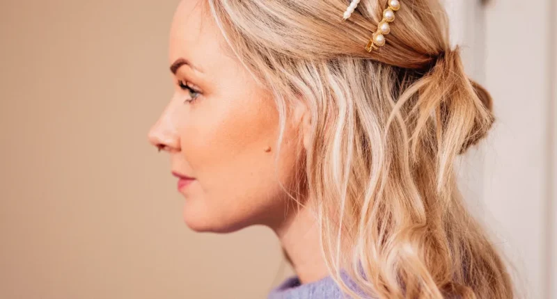 A woman displays a half-up, half-down hairstyle with gentle waves and a twist secured by elegant pearl hair accessories, perfect for a soft and romantic spring look.