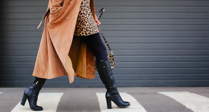 Fashionable woman striding confidently in a leopard print coat paired with black leather boots, creating a statement winter look that combines classic patterns with modern style.