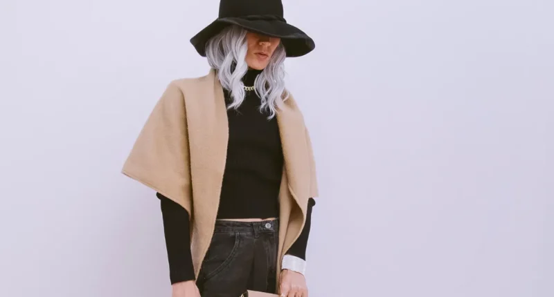 A fashionable winter look with a woman in a black turtleneck, topped with a beige shawl and wide-brimmed hat, paired with black jeans, creating a boho-chic vibe