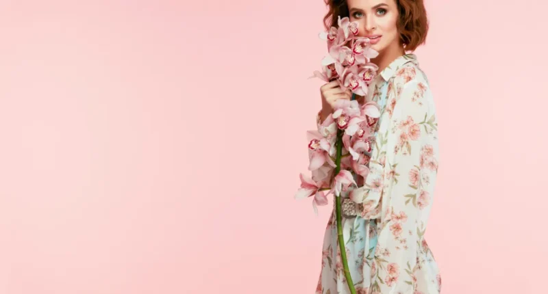 A model holding a bouquet of orchids, wearing a light floral-patterned robe in shades of pink and green, epitomizing the blooming essence of spring fashion trends.