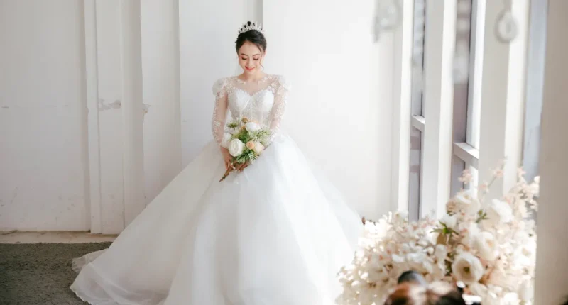 Bride in a pristine white wedding gown with delicate lace sleeves, holding a bouquet, radiating winter wonderland nuptial vibes.