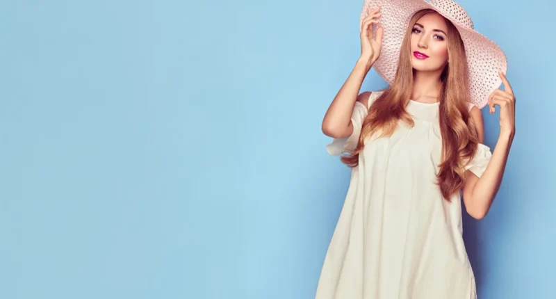 A woman accessorizes her relaxed ivory dress with a wide-brimmed summer hat, embodying a breezy, carefree spring look.