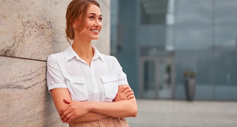 Here, a woman stands confidently outdoors, wearing a timeless white shirt with a modern, sleeveless design, paired with a neutral skirt. The outfit epitomizes classic workwear with a contemporary edge, ideal for a springtime professional wardrobe.